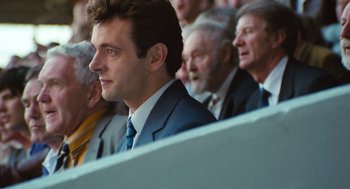 Movie still from “The Damned United” (2009), directed by Tom Hooper – A man in a suit and tie sitting in front of other men; Close Up shot, Over the shoulder angle