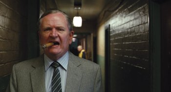 Movie still from “The Damned United” (2009), directed by Tom Hooper – An older man wearing a suit and tie smoking a cigarette; Close Up shot, Low angle