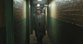 Movie still from “The Damned United” (2009), directed by Tom Hooper – An older man in a coat and hat walking down a hallway; Wide shot, Low angle
