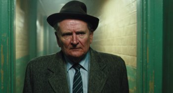 Movie still from “The Damned United” (2009), directed by Tom Hooper – An older man wearing a hat and a suit; Close Up shot, Low angle