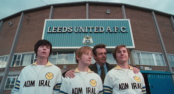 Movie still from “The Damned United” (2009), directed by Tom Hooper – A group of young men standing next to each other in front of a stadium; Wide shot, High angle