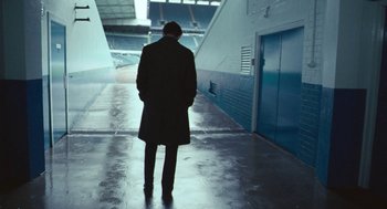 Movie still from “The Damned United” (2009), directed by Tom Hooper – A man in a coat and hat is standing in a tunnel; Wide shot, Low angle