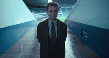 Movie still from “The Damned United” (2009), directed by Tom Hooper – A man in a suit and tie standing in a stadium; Medium shot, High angle