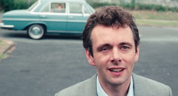 Movie still from “The Damned United” (2009), directed by Tom Hooper – A person wearing a suit near a car; Close Up shot, Over the shoulder angle