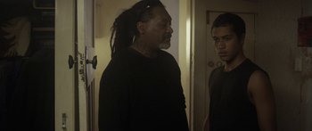 Movie still from “The Dark Horse” (2014), directed by James Napier Robertson – A man with dreadlocks standing next to another man in a doorway; Medium shot, Over the shoulder angle