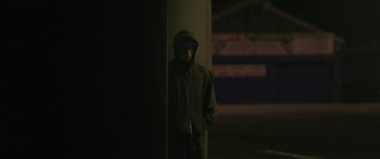 Movie still from “The Dark Horse” (2014), directed by James Napier Robertson – A man in a hooded jacket standing next to a wall; Medium shot, Low angle