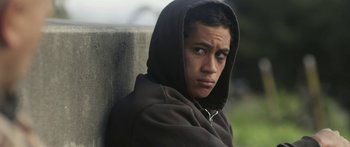 Movie still from “The Dark Horse” (2014), directed by James Napier Robertson – A young man wearing a hooded sweatshirt looks into the distance; Close Up shot, High angle