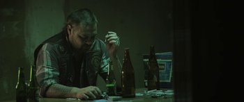 Movie still from “The Dark Horse” (2014), directed by James Napier Robertson – A man sitting at a table in front of a beer bottle; Medium shot, Low angle