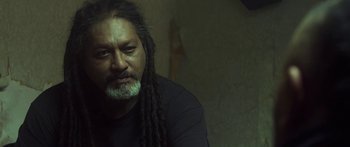 A man with dreadlocks is sitting in front of a wall
