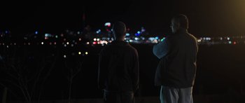 Movie still from “The Dark Horse” (2014), directed by James Napier Robertson – A man standing in front of a city at night; Medium shot, Over the shoulder angle