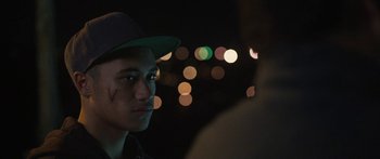 Movie still from “The Dark Horse” (2014), directed by James Napier Robertson – A young man wearing a green hat looking into the distance; Close Up shot, Over the shoulder angle