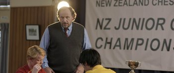 Movie still from “The Dark Horse” (2014), directed by James Napier Robertson – A man standing next to another man in front of a banner; Medium shot, Over the shoulder angle