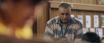 Movie still from “The Dark Horse” (2014), directed by James Napier Robertson – A man with a shaved head is sitting at a table; Medium shot, Over the shoulder angle