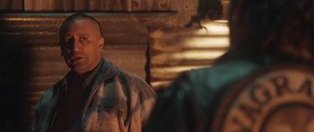 Movie still from “The Dark Horse” (2014), directed by James Napier Robertson – A man wearing a plaid shirt is sitting in front of a log cabin; Close Up shot, Over the shoulder angle