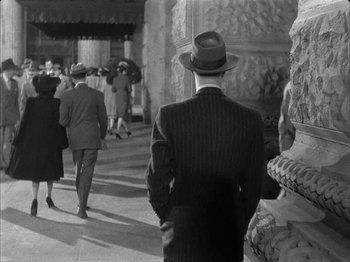 Movie still from “The Dark Mirror” (1946), directed by Robert Siodmak – A man in a suit and a hat walking down a street; Wide shot, Over the shoulder angle
