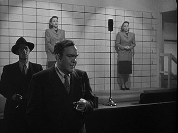 Movie still from “The Dark Mirror” (1946), directed by Robert Siodmak – A man in a suit and tie standing in front of a microphone; Wide shot, Low angle