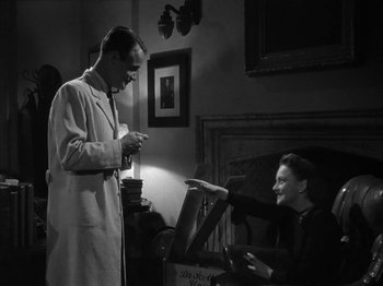 Movie still from “The Dark Mirror” (1946), directed by Robert Siodmak – A man in a lab coat standing next to a woman in an old - fashioned chair; Medium shot, High angle