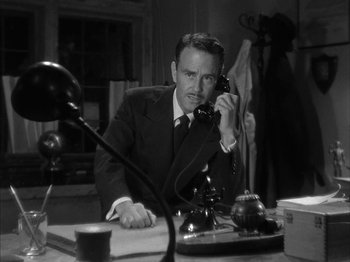Movie still from “The Dark Mirror” (1946), directed by Robert Siodmak – A man sitting at a desk talking on a phone; Medium shot, High angle