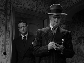 Movie still from “The Dark Mirror” (1946), directed by Robert Siodmak – A man in a suit and a man in a hat looking at a cell phone; Medium shot, Low angle