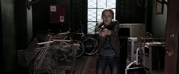 Movie still from “The Darkest Hour” (2011), directed by Chris Gorak – A woman holding a gun in a room full of bicycles; Medium shot, Over the shoulder angle