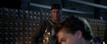 Movie still from “The Darkest Hour” (2011), directed by Chris Gorak – A man wearing a black hat and a metal apron; Medium shot, Over the shoulder angle