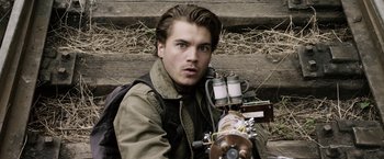 Movie still from “The Darkest Hour” (2011), directed by Chris Gorak – A young man with a backpack holding a machine gun in front of stairs; Close Up shot, High angle