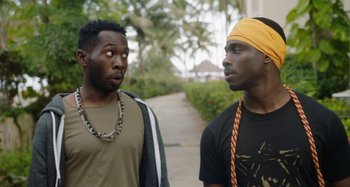 Movie still from “The Day Shall Come” (2019), directed by Christopher Morris – Two men standing next to each other on a sidewalk; Close Up shot, Over the shoulder angle