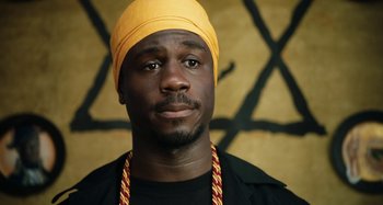 Movie still from “The Day Shall Come” (2019), directed by Christopher Morris – A man wearing a yellow hat and a black shirt; Close Up shot, Low angle