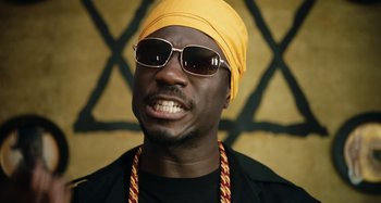 Movie still from “The Day Shall Come” (2019), directed by Christopher Morris – A person wearing sunglasses and a turban; Close Up shot, Low angle