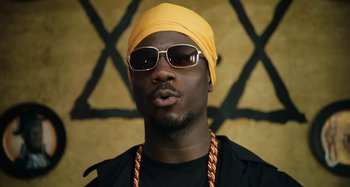 Movie still from “The Day Shall Come” (2019), directed by Christopher Morris – A person wearing sunglasses and a turban; Close Up shot, Low angle