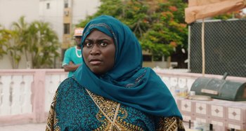 Movie still from “The Day Shall Come” (2019), directed by Christopher Morris – A woman wearing a head scarf standing in front of a building; Close Up shot, Over the shoulder angle