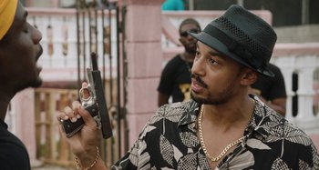 Movie still from “The Day Shall Come” (2019), directed by Christopher Morris – A man holding a gun while wearing a hat; Close Up shot, Over the shoulder angle