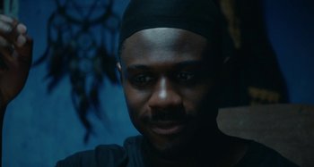 Movie still from “The Day Shall Come” (2019), directed by Christopher Morris – A person wearing a black hat; Close Up shot, Low angle