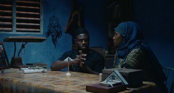 Movie still from “The Day Shall Come” (2019), directed by Christopher Morris – A man and a woman sitting at a table talking to each other; Medium shot, Over the shoulder angle