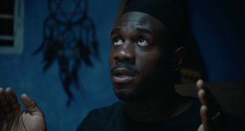 Movie still from “The Day Shall Come” (2019), directed by Christopher Morris – A person wearing a black hat; Close Up shot, Low angle
