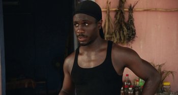 Movie still from “The Day Shall Come” (2019), directed by Christopher Morris – A man in a black tank top and a black hat; Medium shot, Low angle