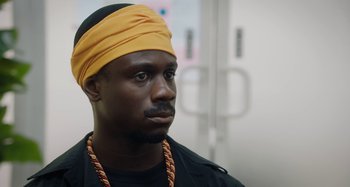 Movie still from “The Day Shall Come” (2019), directed by Christopher Morris – A black man with a yellow head band on; Close Up shot, Over the shoulder angle
