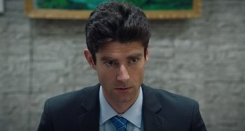 Movie still from “The Day Shall Come” (2019), directed by Christopher Morris – A person wearing a suit and tie; Close Up shot, Over the shoulder angle