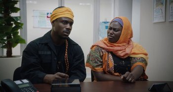 Movie still from “The Day Shall Come” (2019), directed by Christopher Morris – A man and a woman sitting at a table; Medium shot, Over the shoulder angle