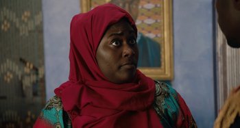 Movie still from “The Day Shall Come” (2019), directed by Christopher Morris – A woman in a red head scarf stares into the distance; Close Up shot, Over the shoulder angle