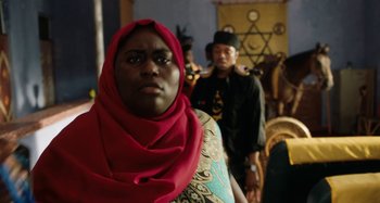 Movie still from “The Day Shall Come” (2019), directed by Christopher Morris – A woman in a red head scarf standing in front of other people; Close Up shot, Over the shoulder angle