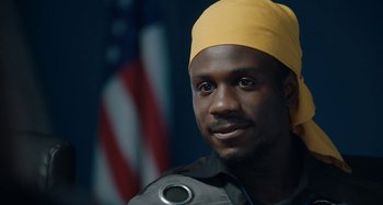 Movie still from “The Day Shall Come” (2019), directed by Christopher Morris – A person wearing a yellow hat; Close Up shot, Over the shoulder angle