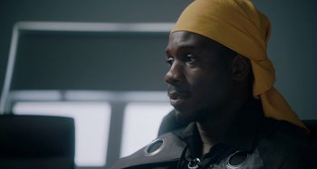 Movie still from “The Day Shall Come” (2019), directed by Christopher Morris – A person wearing a yellow hat; Close Up shot, Over the shoulder angle