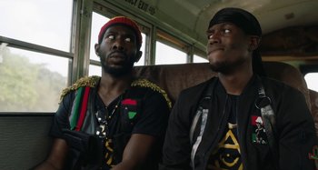 Movie still from “The Day Shall Come” (2019), directed by Christopher Morris – A couple of men sitting next to each other on top of a bus; Close Up shot, Over the shoulder angle