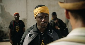 Movie still from “The Day Shall Come” (2019), directed by Christopher Morris – A man wearing a yellow head band and a black shirt; Close Up shot, Over the shoulder angle