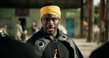 Movie still from “The Day Shall Come” (2019), directed by Christopher Morris – A man with a yellow head band is posing for a picture; Close Up shot, Over the shoulder angle