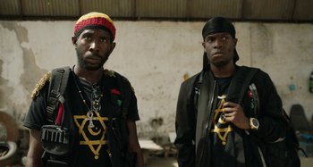 Movie still from “The Day Shall Come” (2019), directed by Christopher Morris – A couple of men standing next to each other; Medium shot, Over the shoulder angle