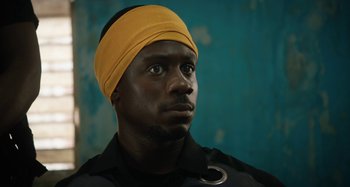 Movie still from “The Day Shall Come” (2019), directed by Christopher Morris – A man wearing a yellow head band and a black shirt; Close Up shot, Low angle