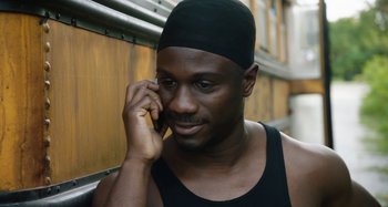Movie still from “The Day Shall Come” (2019), directed by Christopher Morris – A man with a black hat talking on a cell phone; Close Up shot, High angle