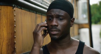 Movie still from “The Day Shall Come” (2019), directed by Christopher Morris – A man with a black hat is talking on a cell phone; Close Up shot, High angle